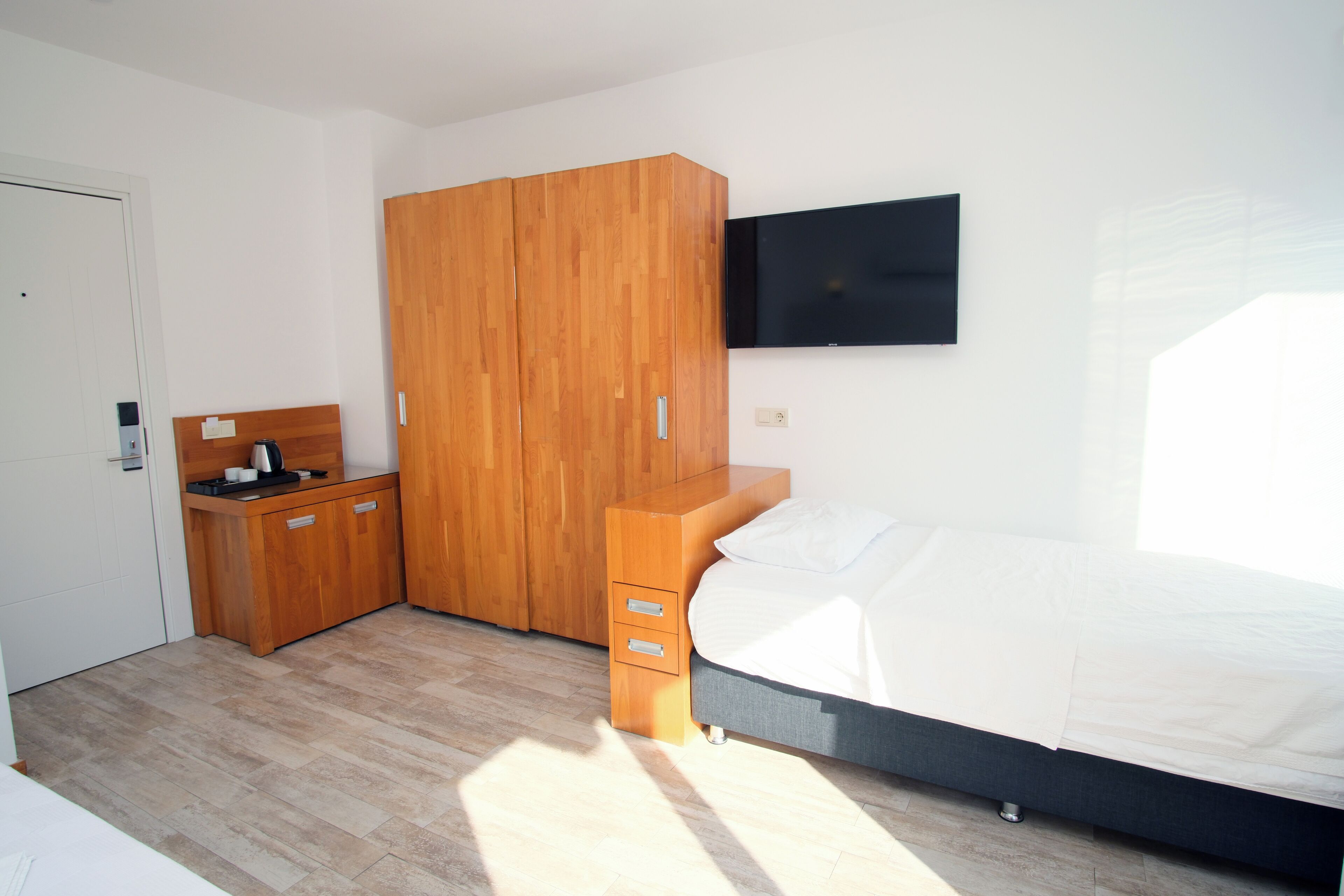 Un dormitorio con cama, armario de madera, un pequeño escritorio con silla y televisor de pantalla plana montado en la pared.