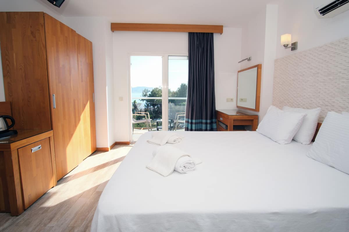 Ein Hotelzimmer mit einem großen Bett, einem Holzschrank, einem Schreibtisch mit Stuhl, einem Spiegel und Blick ins Freie.