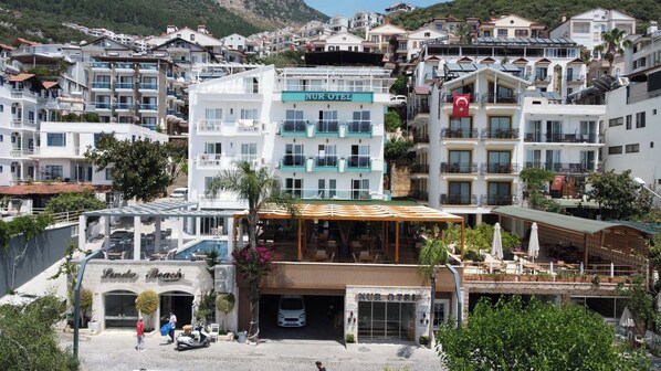 A hotel with a sign reading "NUR OTEL" in a coastal town with buildings in the background. - Nur Hotel (Kas)