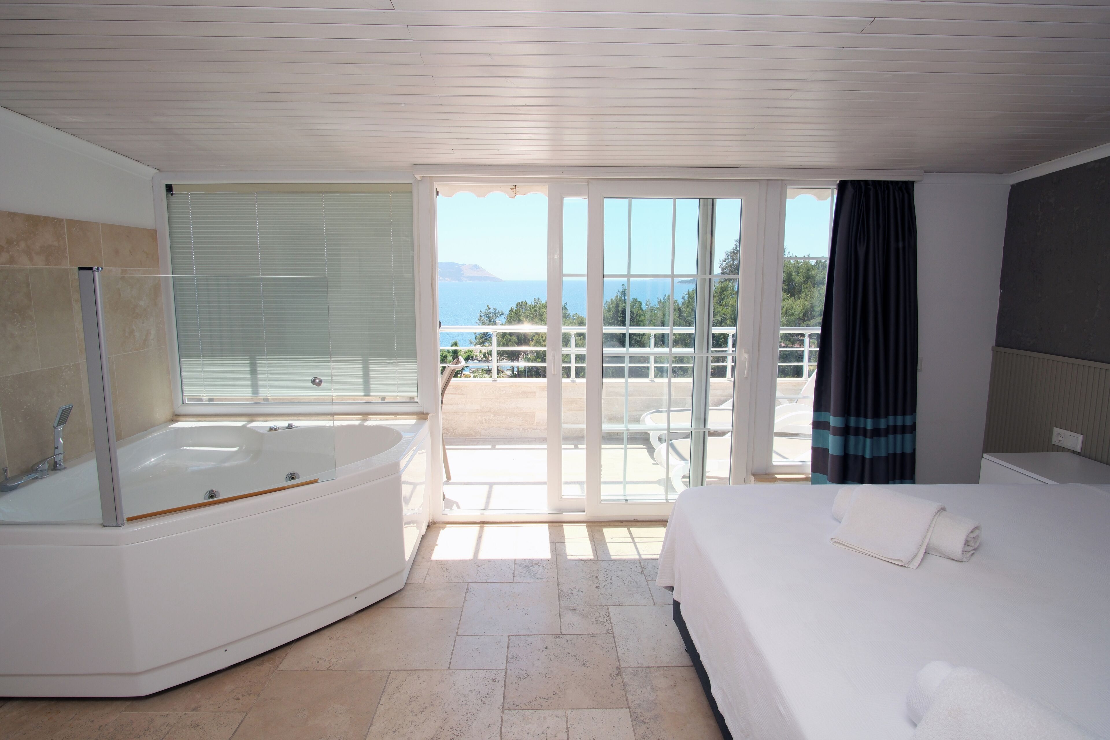 Una habitación de hotel moderna con una bañera grande, una cama y un balcón con vistas al mar.