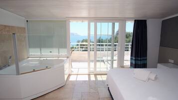Una habitación de hotel moderna con una bañera grande, una cama y un balcón con vistas al mar.