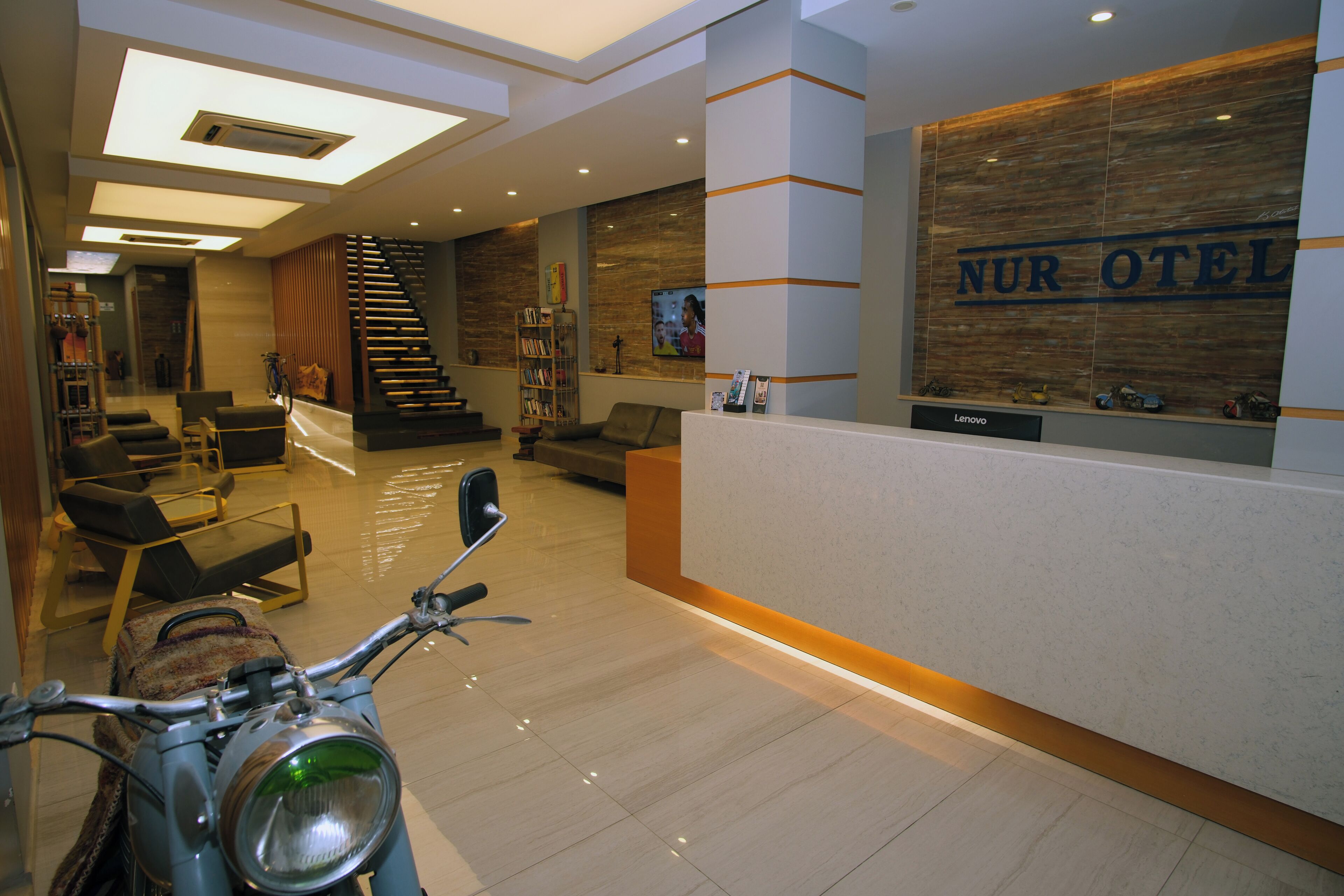 A hotel reception area with a reception desk, a staircase, and a seating area with chairs and a sofa.