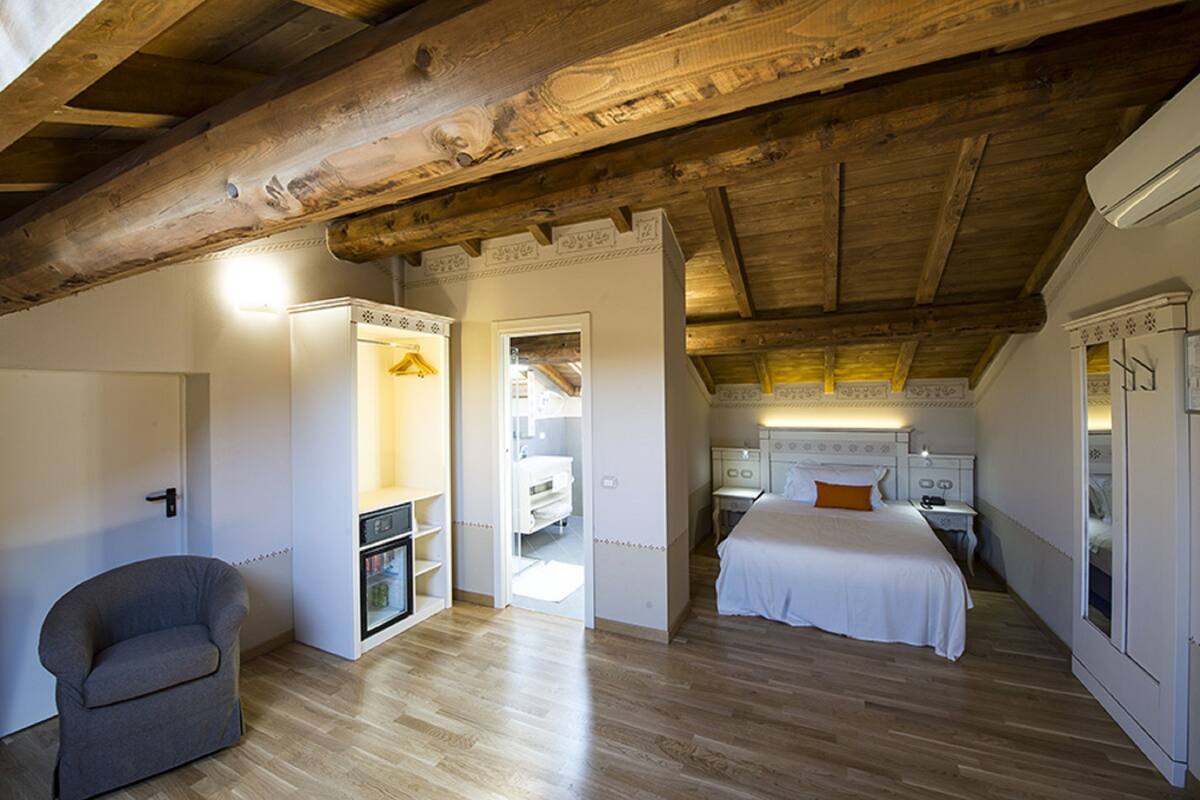 Un dormitorio con techo de madera, una cama, una mesita de noche, una silla y un armario.