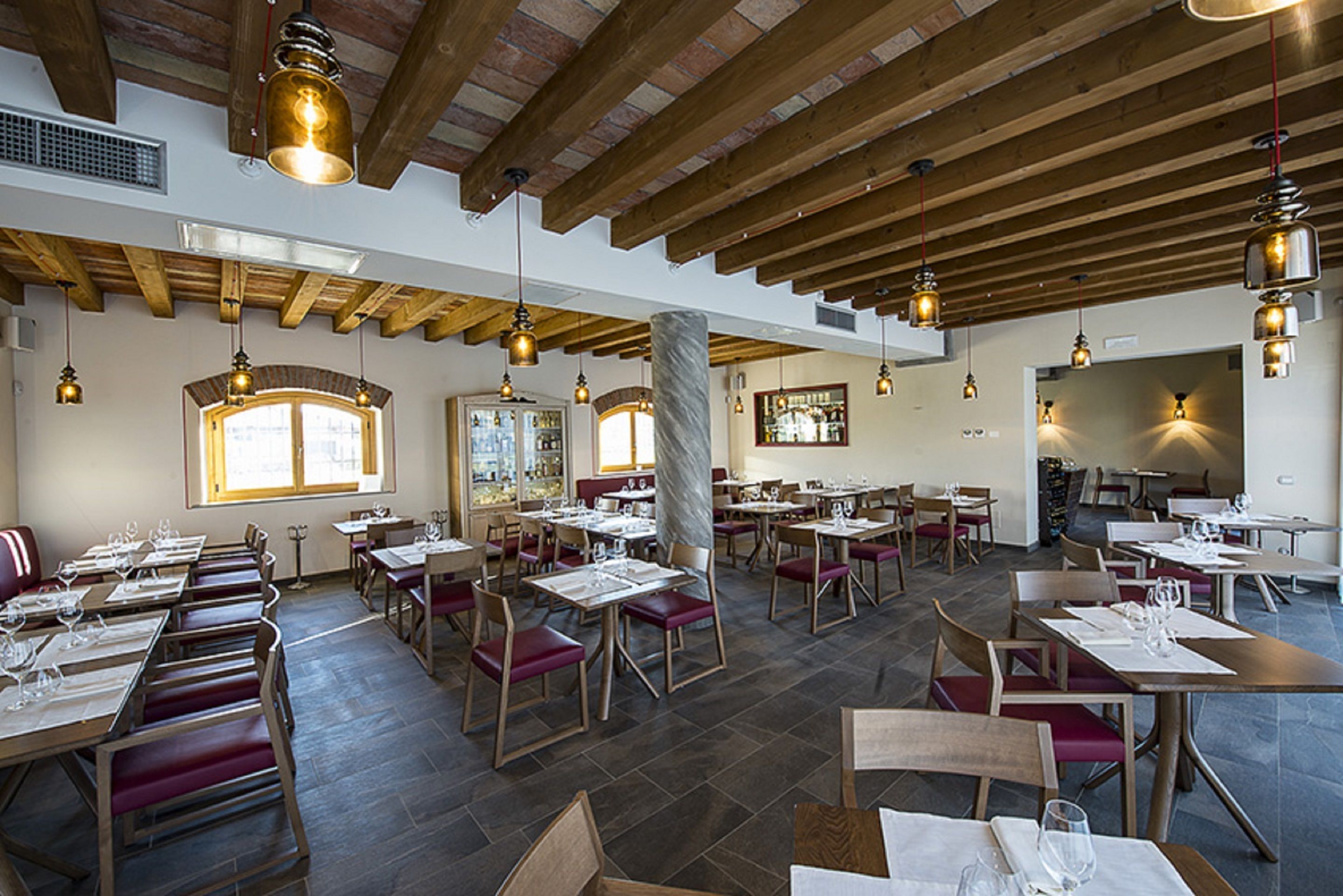 Un restaurante con vigas de madera, columnas de mármol e iluminación colgante. Las mesas están dispuestas con manteles blancos y sillas rojas.