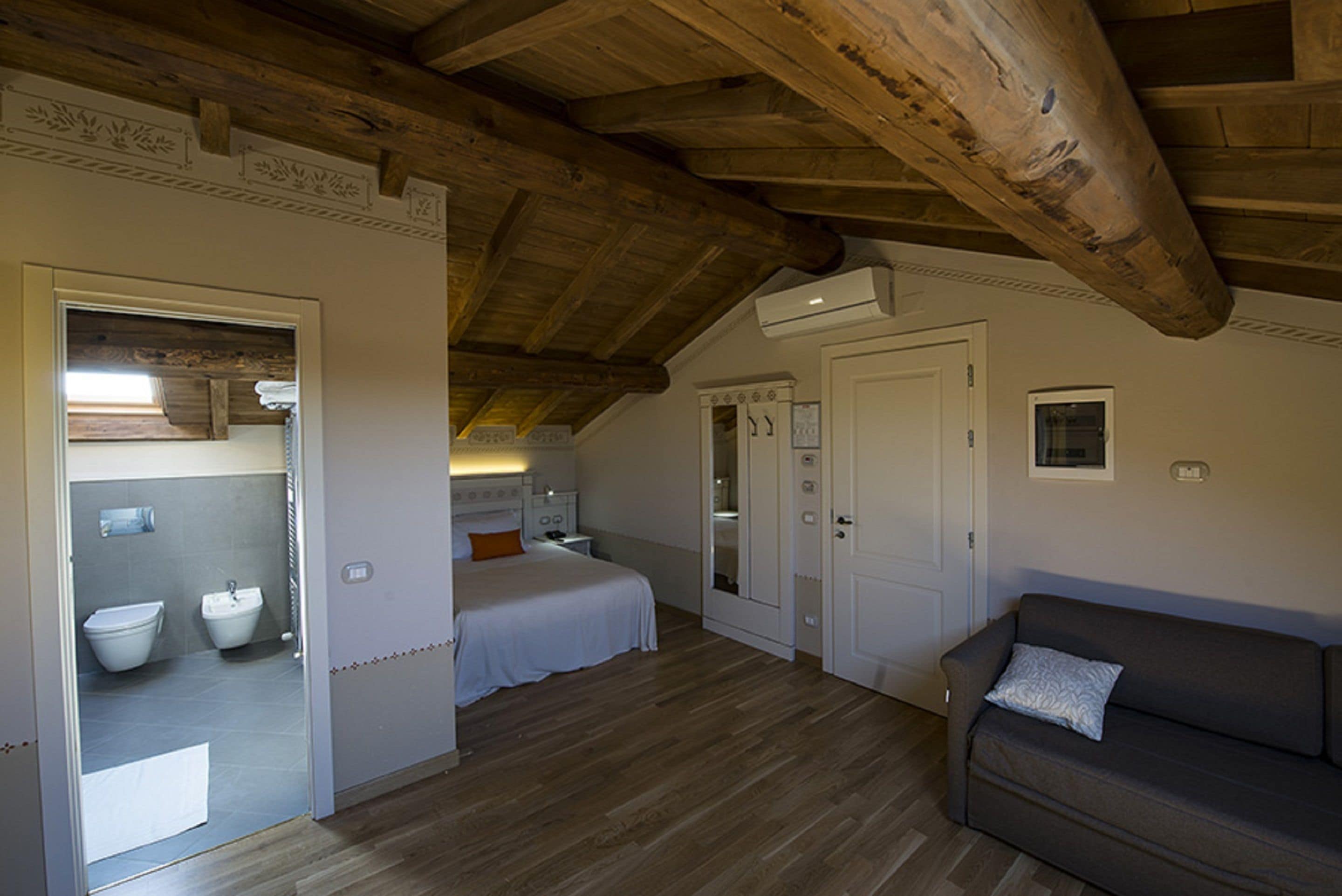 A bedroom with a wooden ceiling, a bed, a nightstand, a dresser, and a bathroom with a toilet and sink.