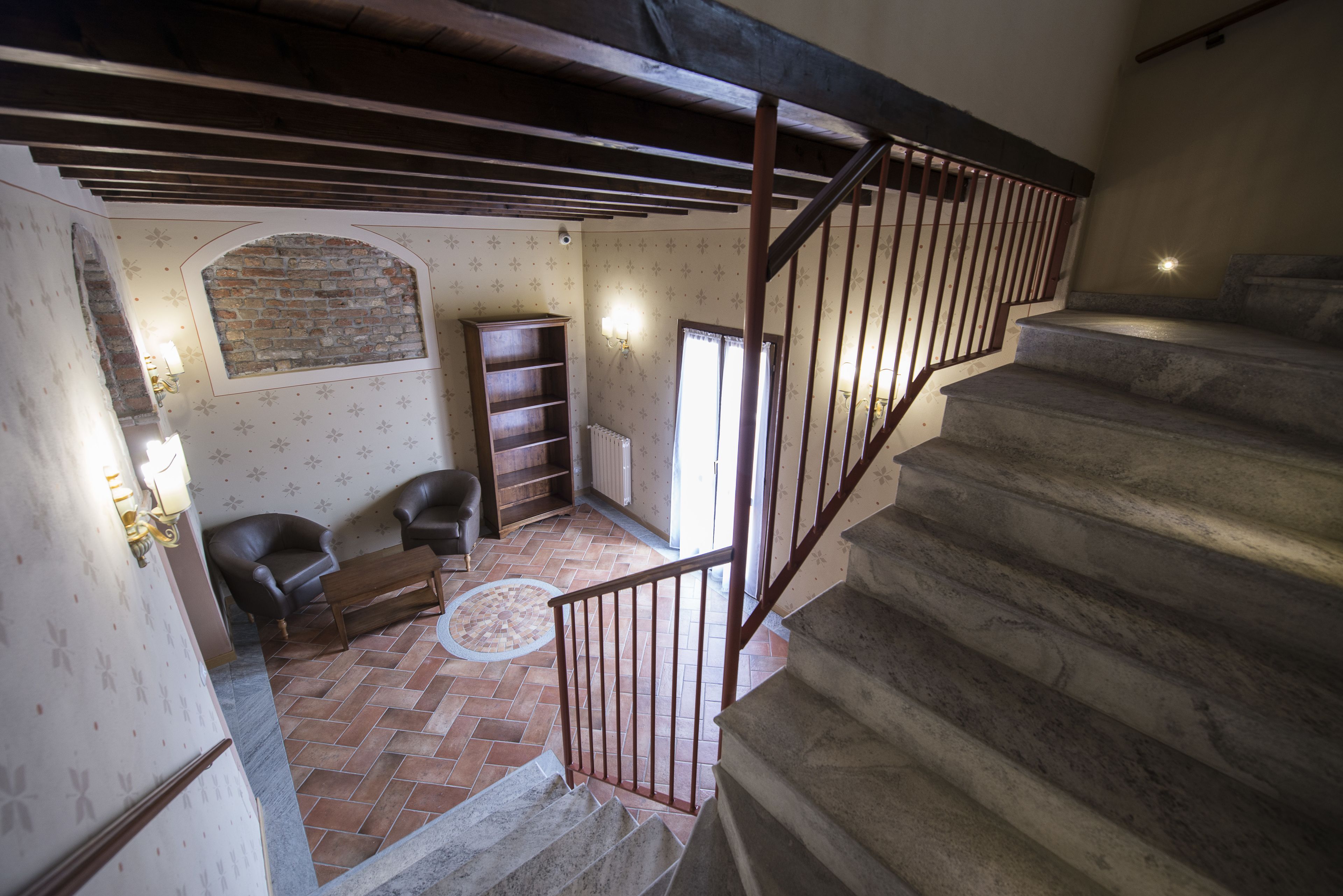 Una escalera conduce a una habitación con suelo de ladrillo, chimenea y estantería de madera.