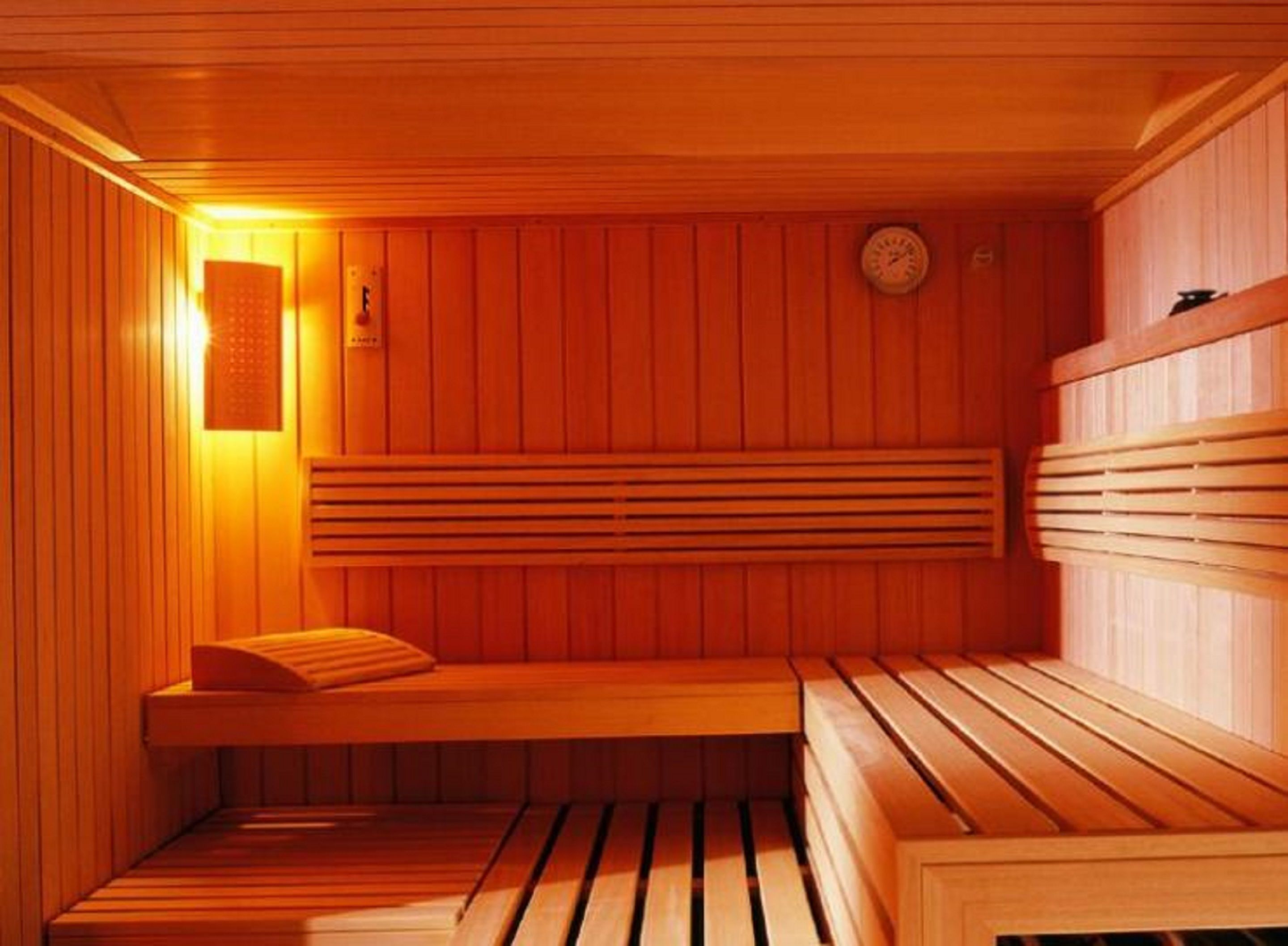 Una sauna con bancos de madera y un asiento, un calentador en la pared y un reloj.