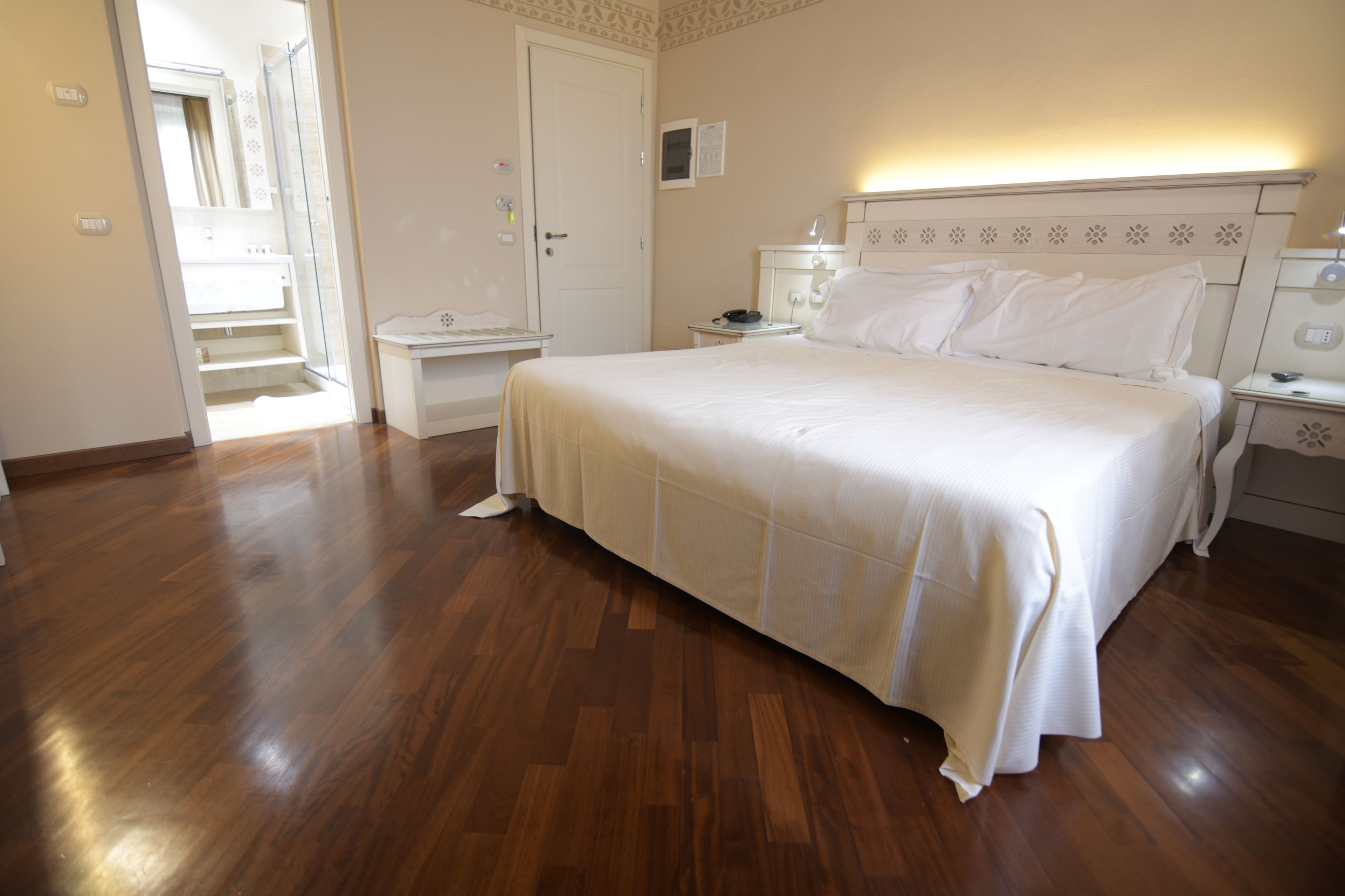 A bedroom with a large bed, bedside tables, and a nightstand. There is a door leading to another room and a small table with a chair.