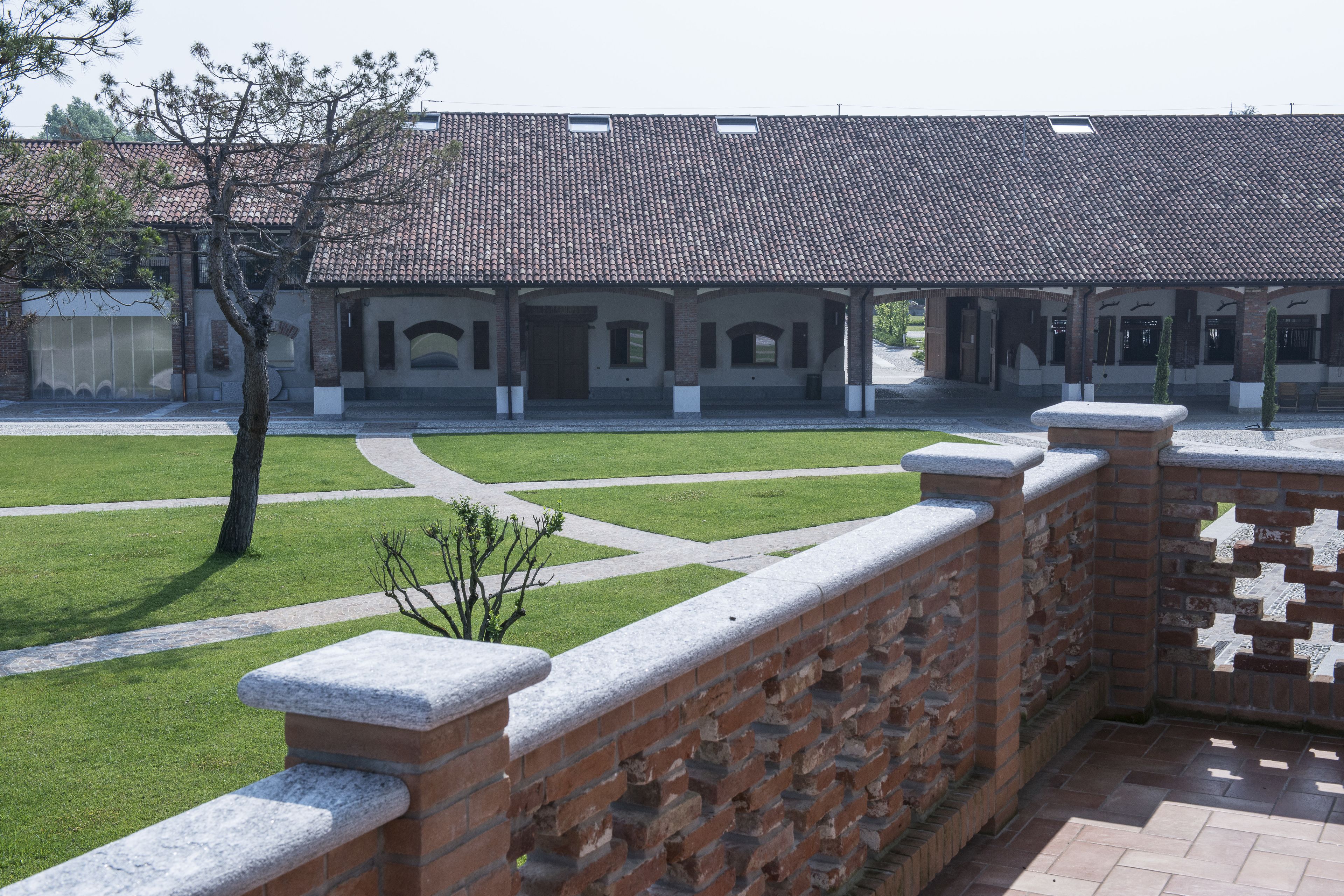 A courtyard with a brick wall, a covered walkway, and a building with a tiled roof.