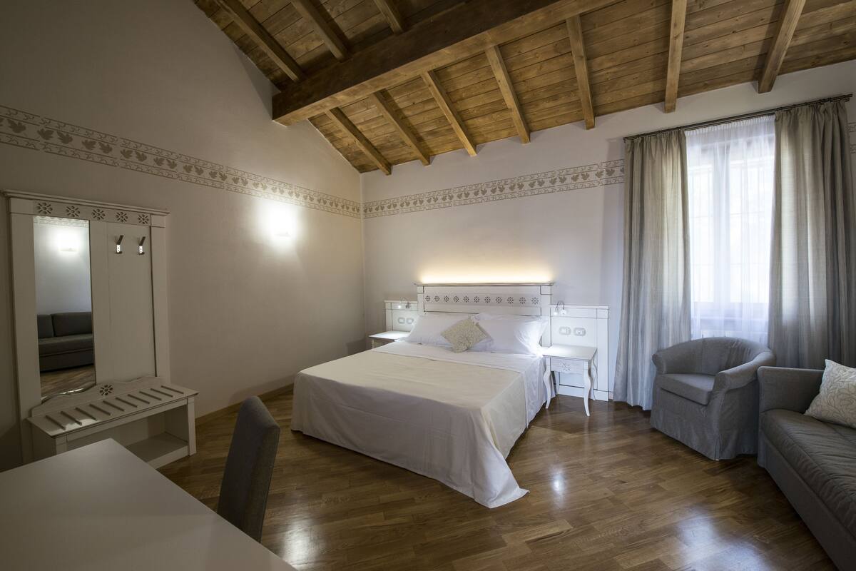 Un dormitorio con techo de madera, una cama, una silla, una mesita de noche, un aparador y un espejo.