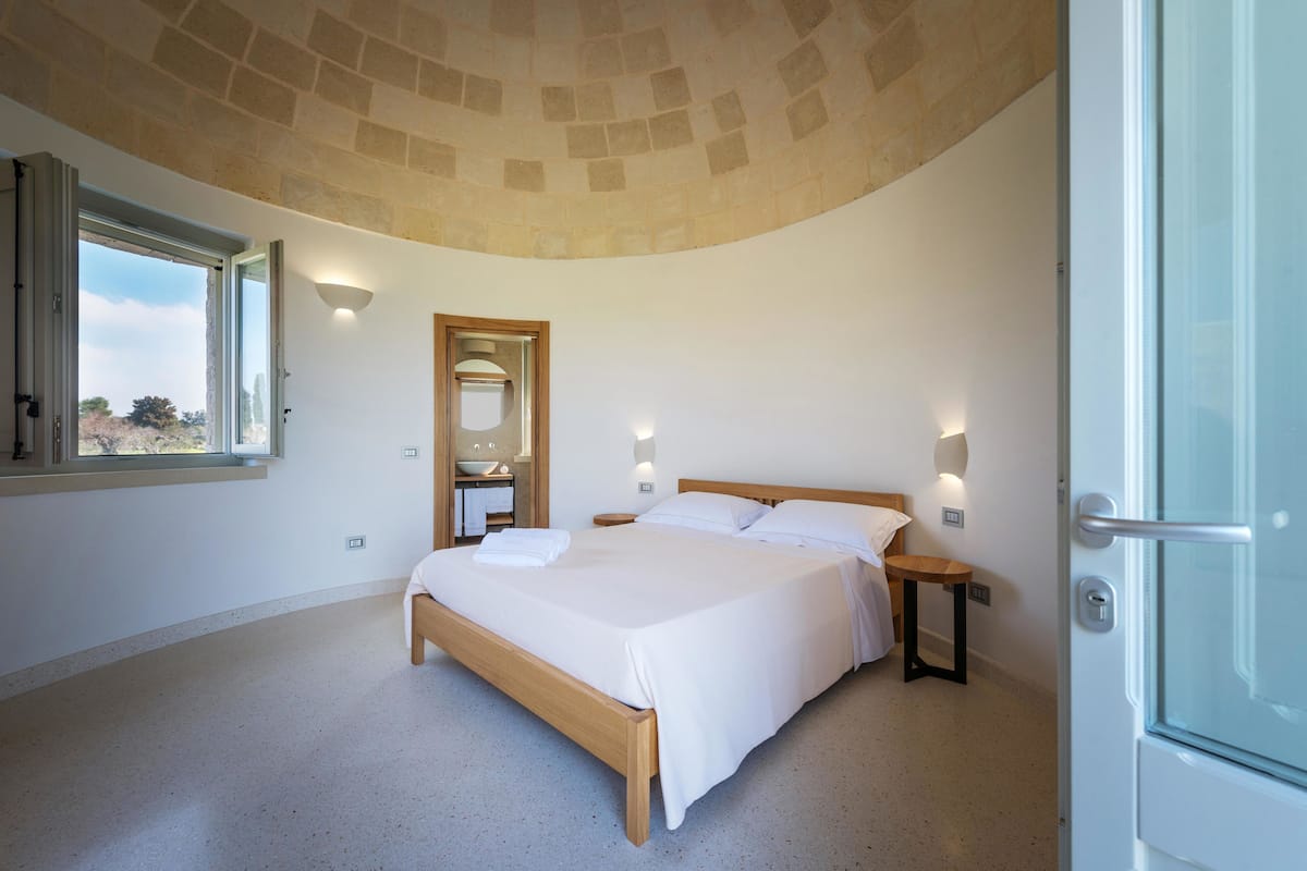 A bedroom with a large bed, a window, a mirror, and a door.