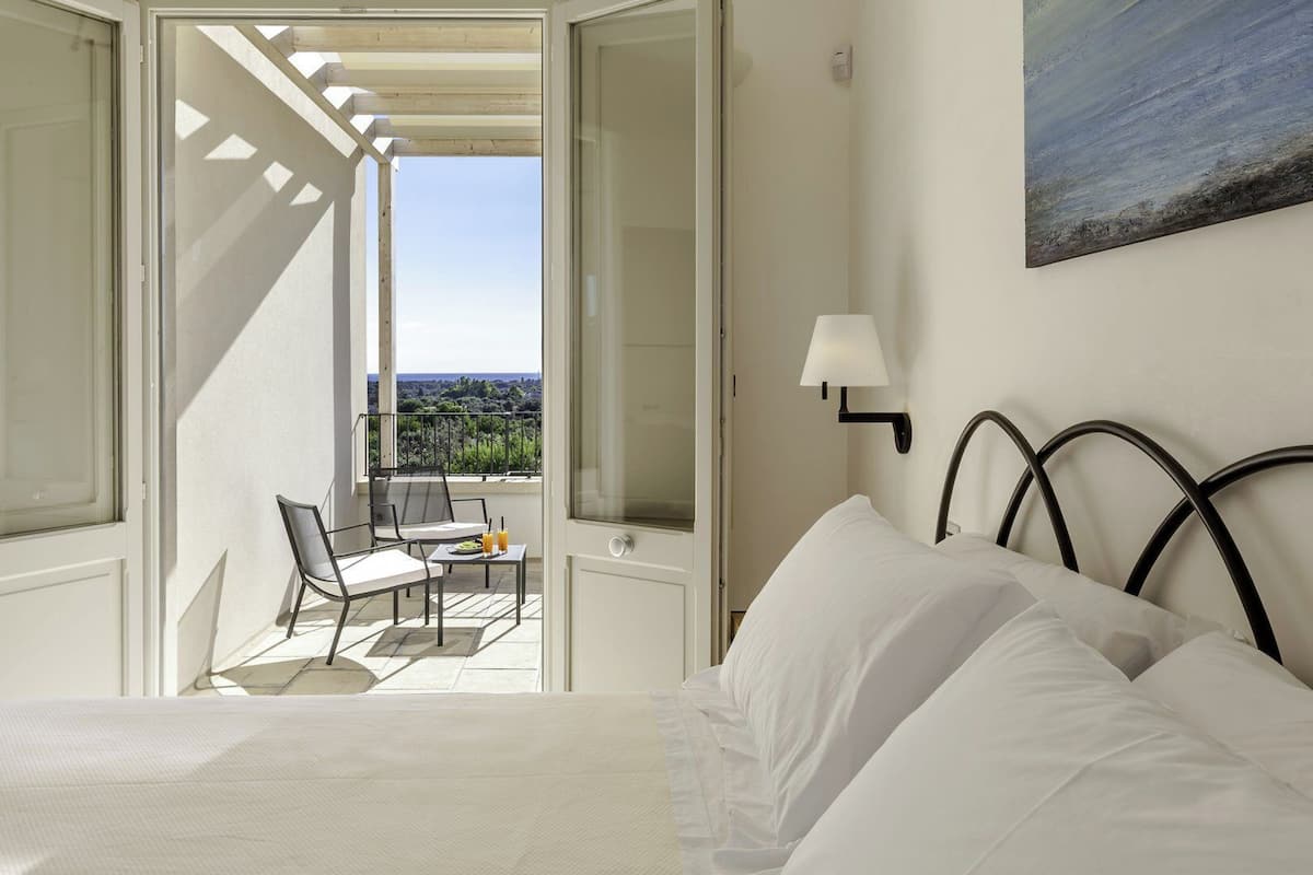 A bedroom with a bed, a nightstand, a lamp, and a view of the outdoors.