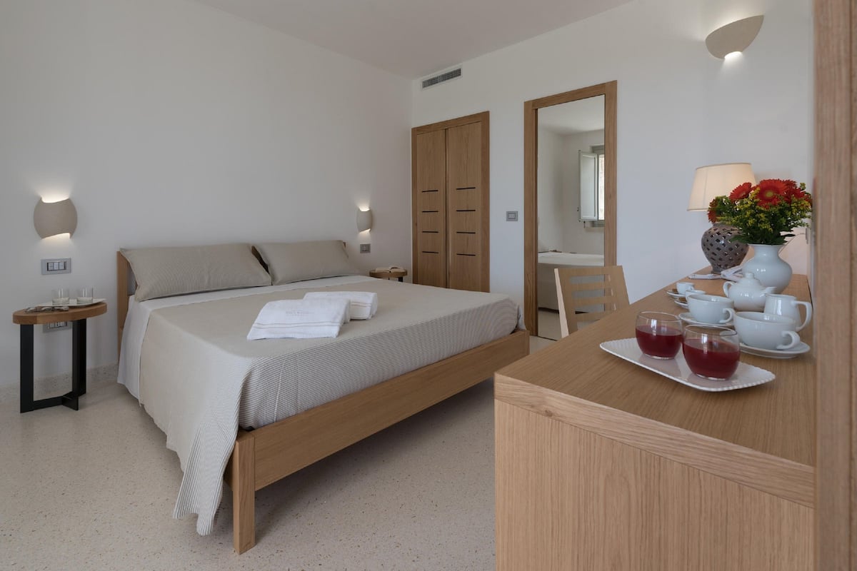 A modern bedroom with a wooden bed, bedside tables, a mirror, and a small table with cups and a vase of flowers.