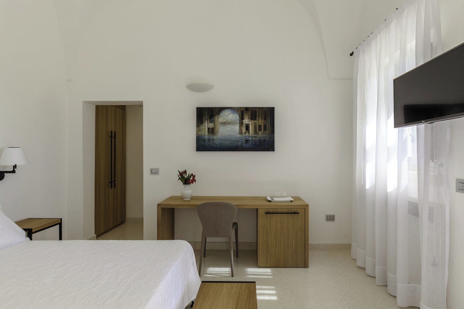 Een hotelkamer met een bed, een bureau, een stoel, een schilderij en een televisie.