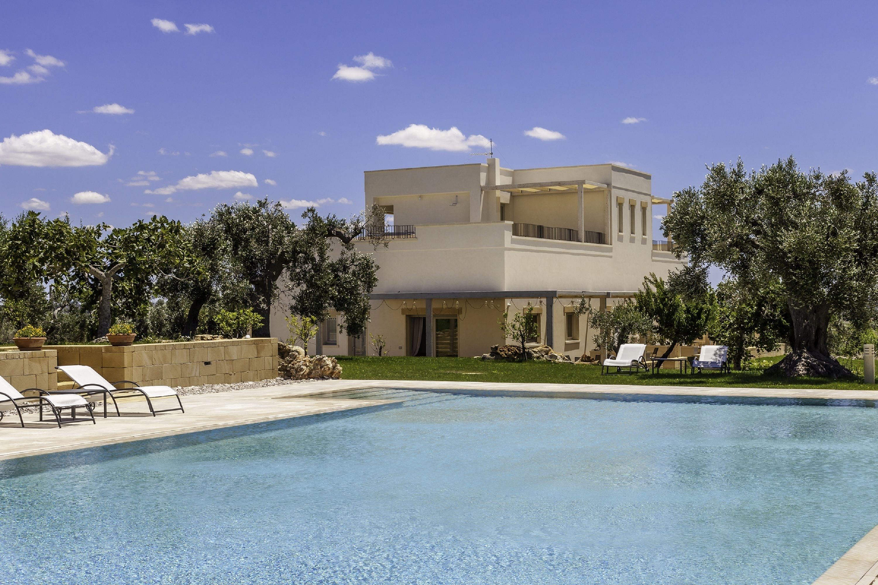 Una casa moderna de dos pisos con piscina, rodeada de árboles y un cielo despejado.