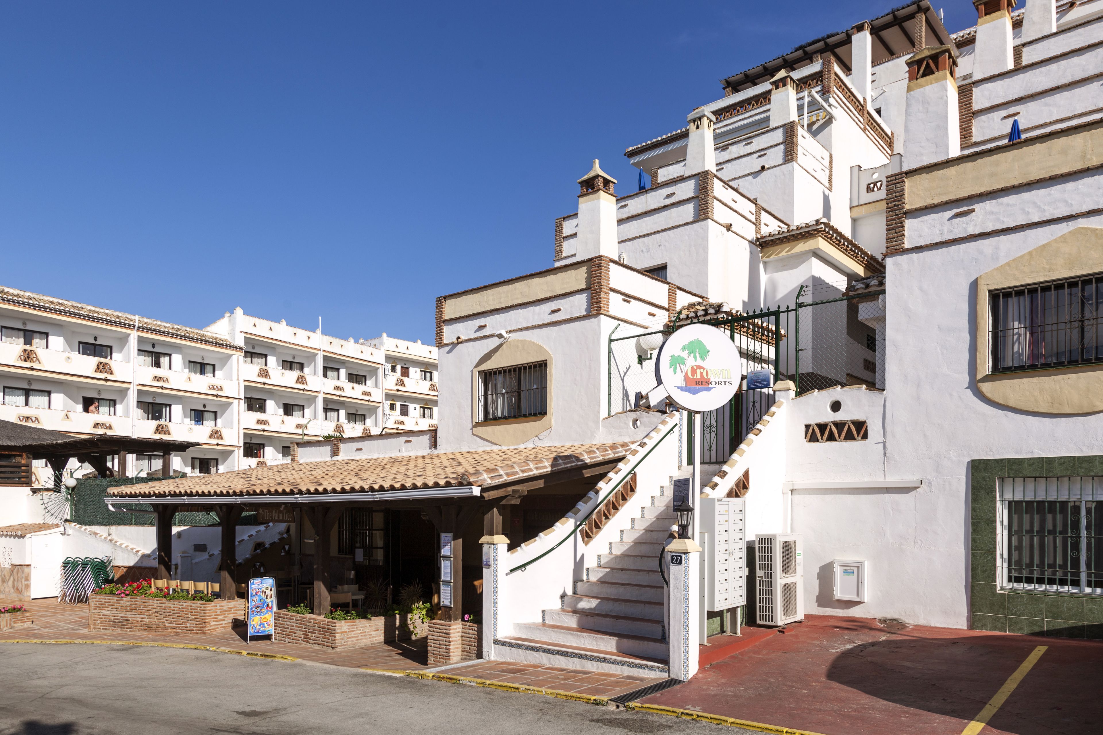 Entrada de un hotel con un porche cubierto, una escalera y un letrero que indica 'Resort'.