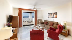 A living room with a sofa, two red chairs, a coffee table, a TV, and a fireplace. - Crown Resorts Club Calahonda (Mijas)