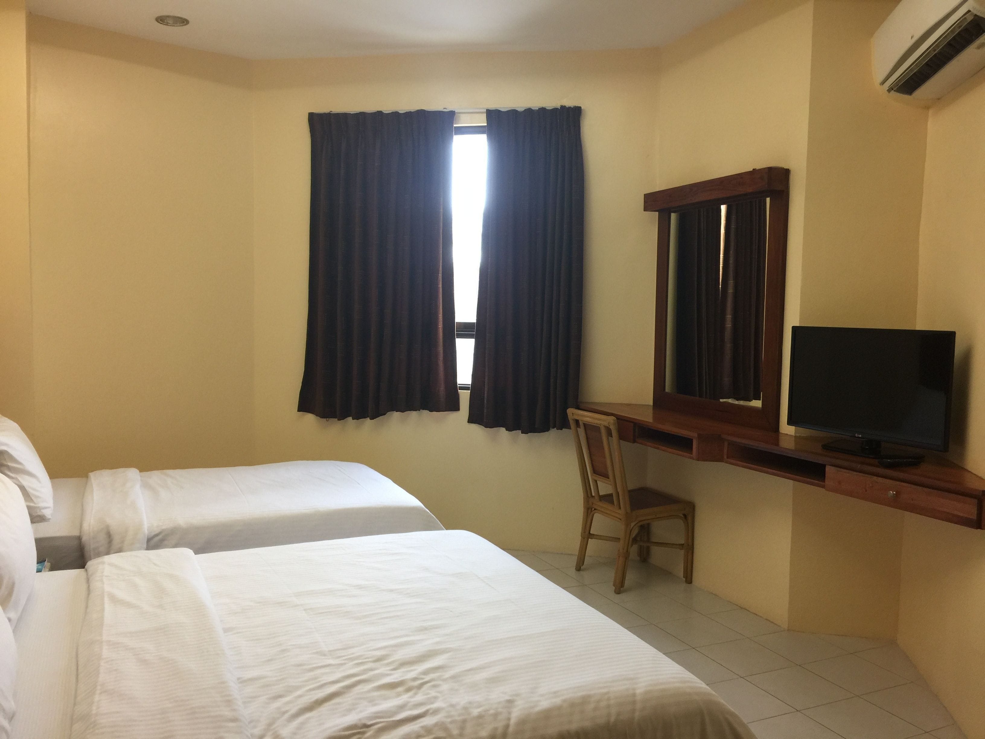 A hotel room with two beds, a desk with a chair, a television, and an air conditioning unit.