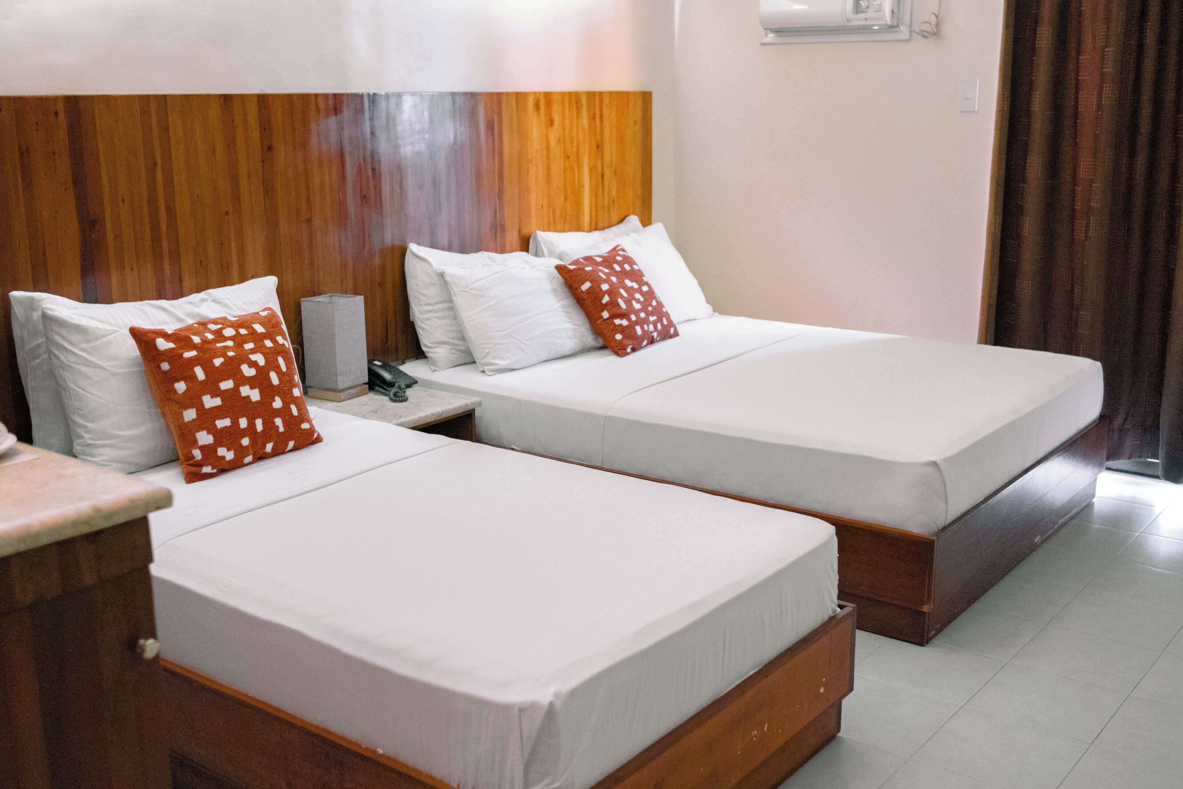 A hotel room with two single beds, each with white bedding and a wooden headboard. There is a nightstand with a lamp and a telephone.