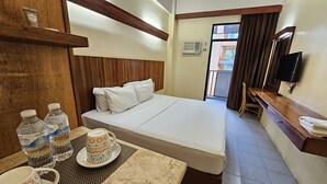 A hotel room with a bed, a table with water bottles and a cup, a TV, and a window with curtains. - Tsai Hotel and Residences (Cebu City)
