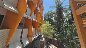 A multi-story building with orange and white exterior walls, balconies, and a view of palm trees and greenery. - Tsai Hotel and Residences (Cebu City)