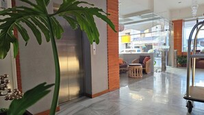 A modern lobby with a large potted plant, a reception desk, and a seating area with wicker furniture. - Tsai Hotel and Residences (Cebu City)