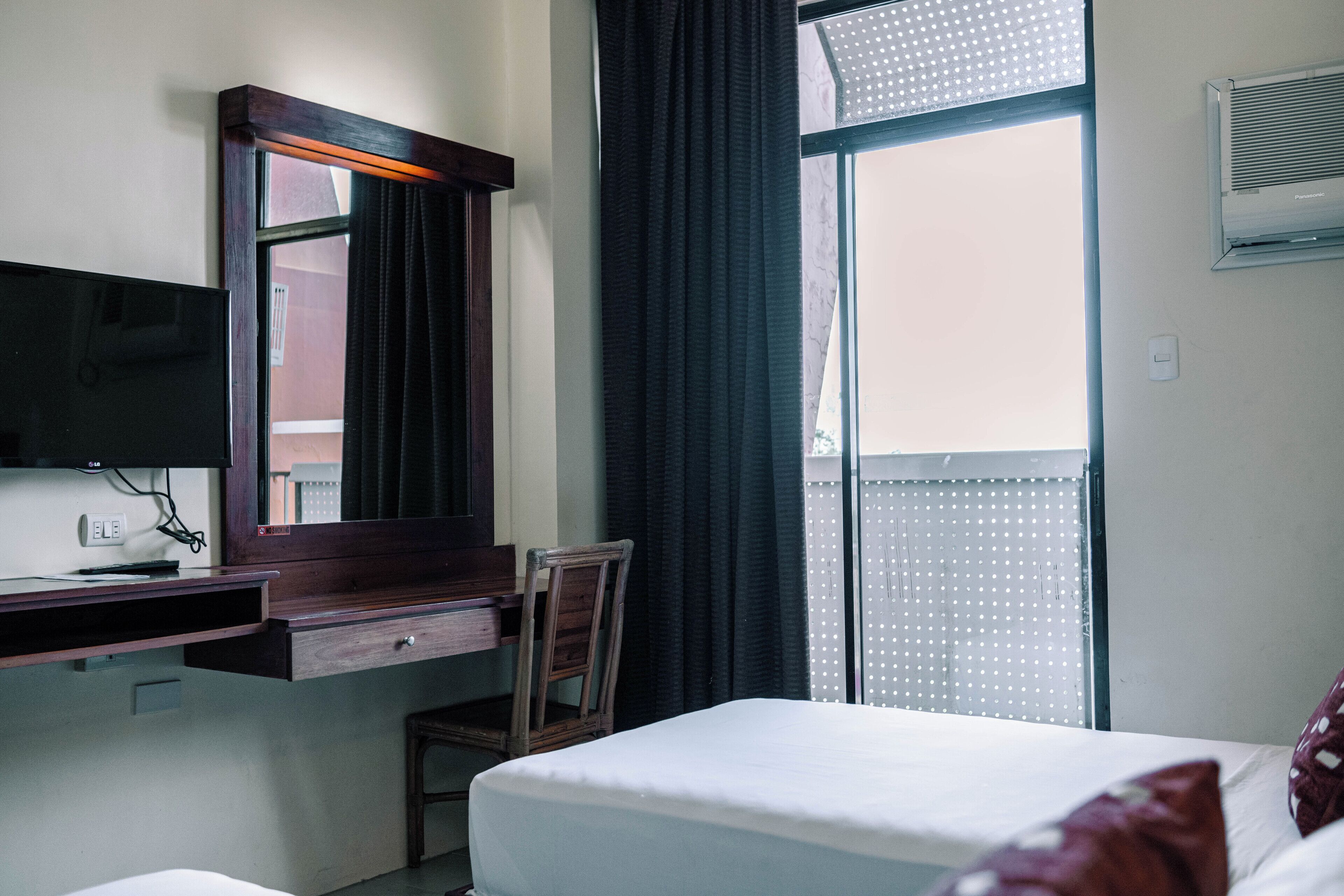 A hotel room with a bed, a desk with a chair, a TV, and a window with curtains.