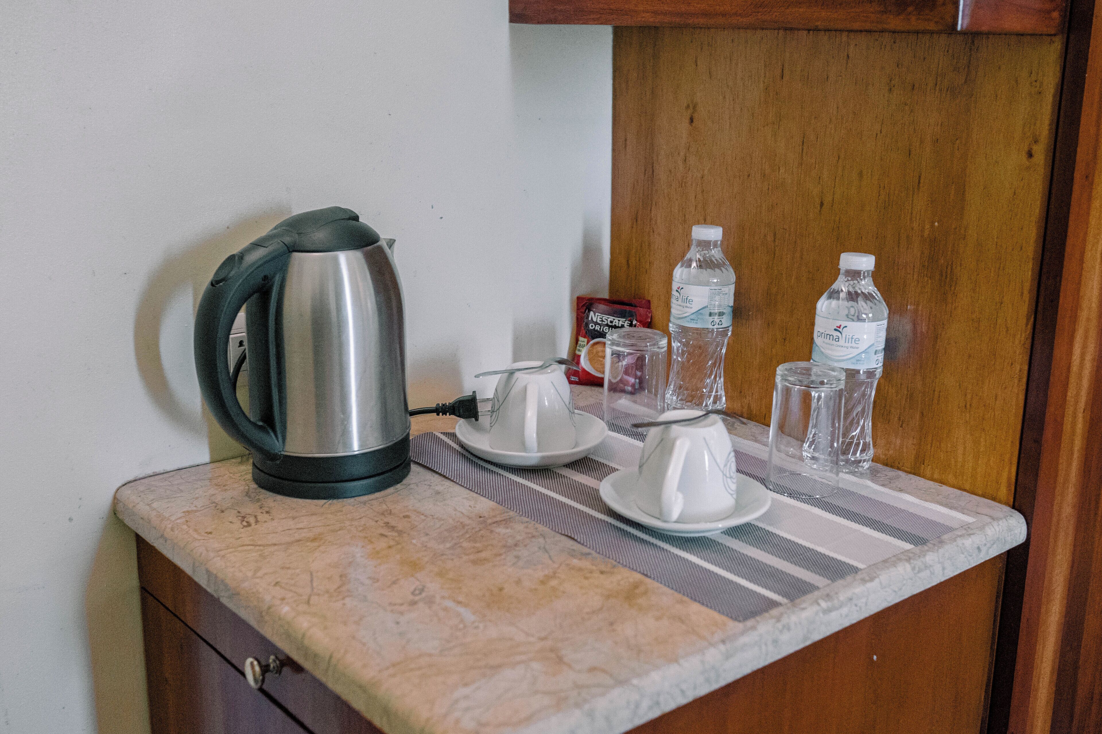 A kitchen counter with a kettle, teapot, cups, and bottled water.