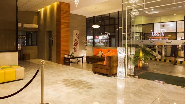 A hotel lobby with a reception desk, a seating area with a sofa and armchairs, a staircase leading to the upper floor, and a chandelier. - Tsai Hotel and Residences (Cebu City)