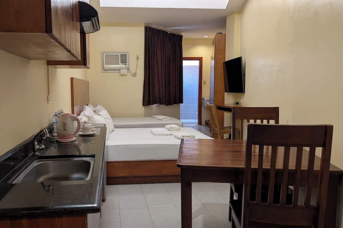 A hotel room with a kitchenette, a bed, a desk, and a TV.