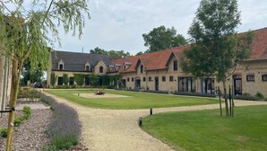 A courtyard with a gravel path, a lawn, and a building with a tiled roof. - Groot Noordhof (Nieuwpoort)