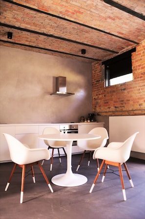 Una cocina moderna con pared de ladrillo, una mesa redonda y cuatro sillas blancas con patas de madera.