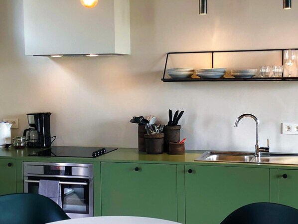 Una cocina compacta con horno empotrado, cafetera y lavamanos.
