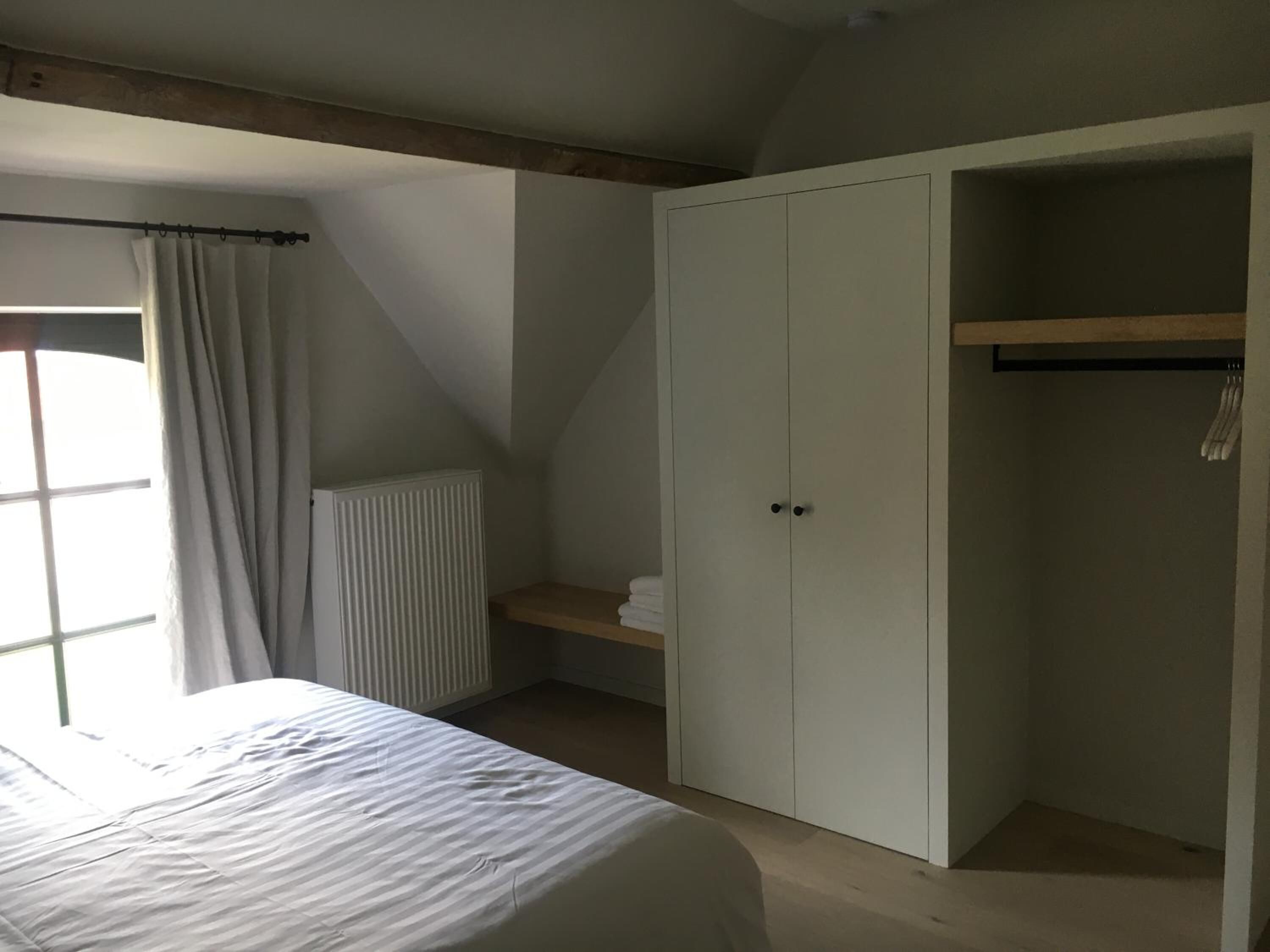 A bedroom with a bed, a wardrobe, a radiator, and a window with curtains.