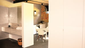A modern bathroom with a large bathtub, a sink, and a shower. There is a brick wall and a white cabinet. - Groot Noordhof (Nieuwpoort)