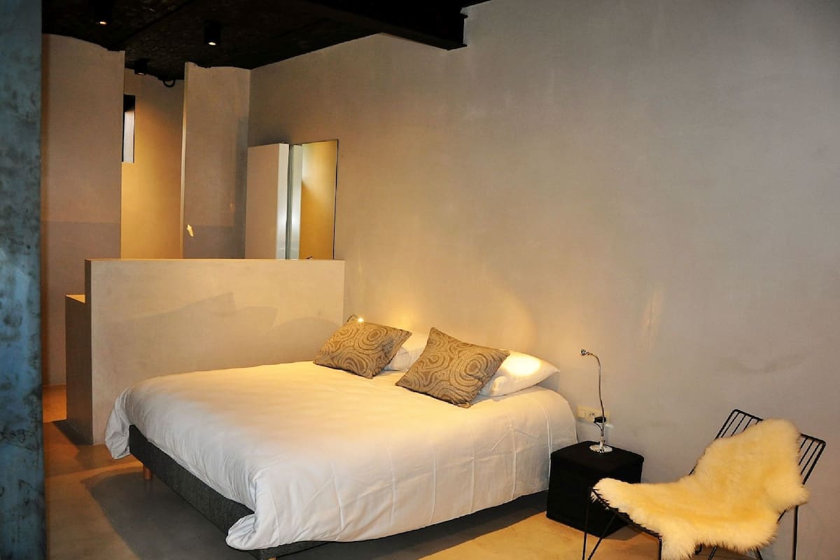 Une chambre moderne avec un grand lit, deux oreillers, une table de chevet avec une lampe et une chaise.