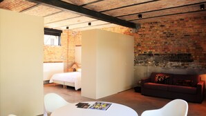 A room with a brick wall, a bed, a sofa, and a table with magazines. - Groot Noordhof (Nieuwpoort)