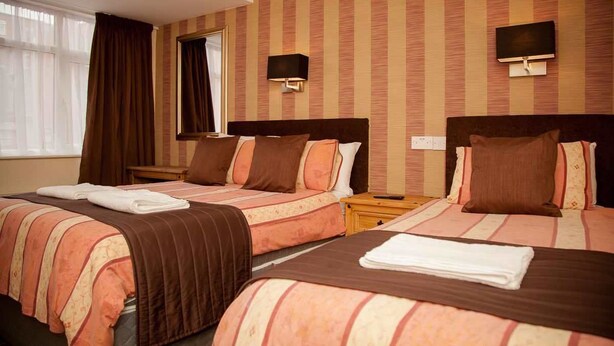 A hotel room with two beds, striped bedding, a flat-screen TV, and a window with curtains. - The Trafford Hotel (Blackpool)