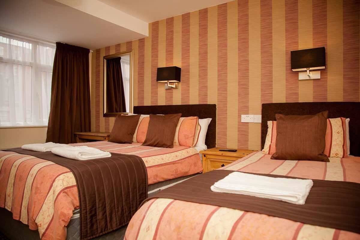 A hotel room with two beds, striped bedding, a flat-screen TV, and a window with curtains.