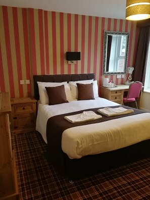 Una camera d'albergo con un letto grande, un comodino, una sedia, una scrivania, uno specchio e una televisione.