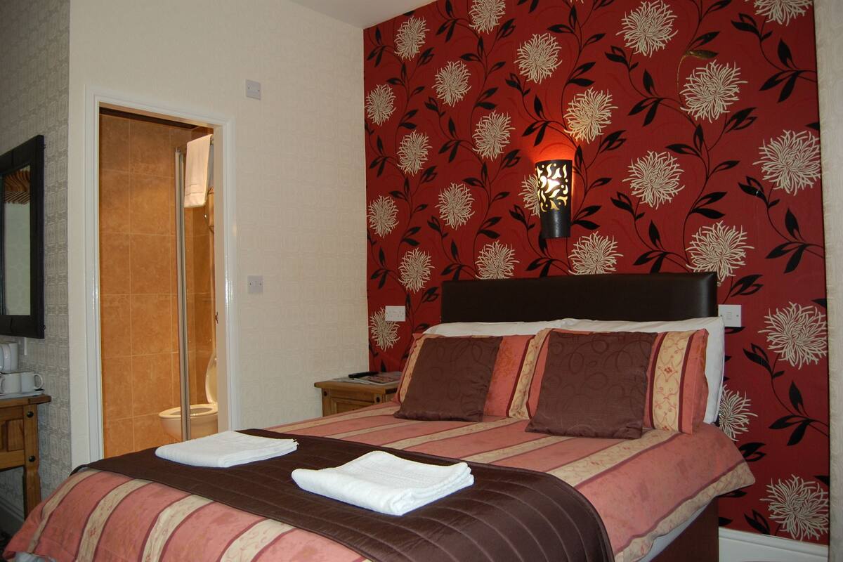 A hotel room with a bed, a nightstand, a lamp, and a shower area.