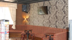 A room with a patterned wallpaper, a television mounted on the wall, a red and white patterned sofa, and a jukebox. - The Trafford Hotel (Blackpool)