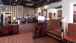 A bar area with a counter, multiple stools, a television, and a vending machine. - The Trafford Hotel (Blackpool)