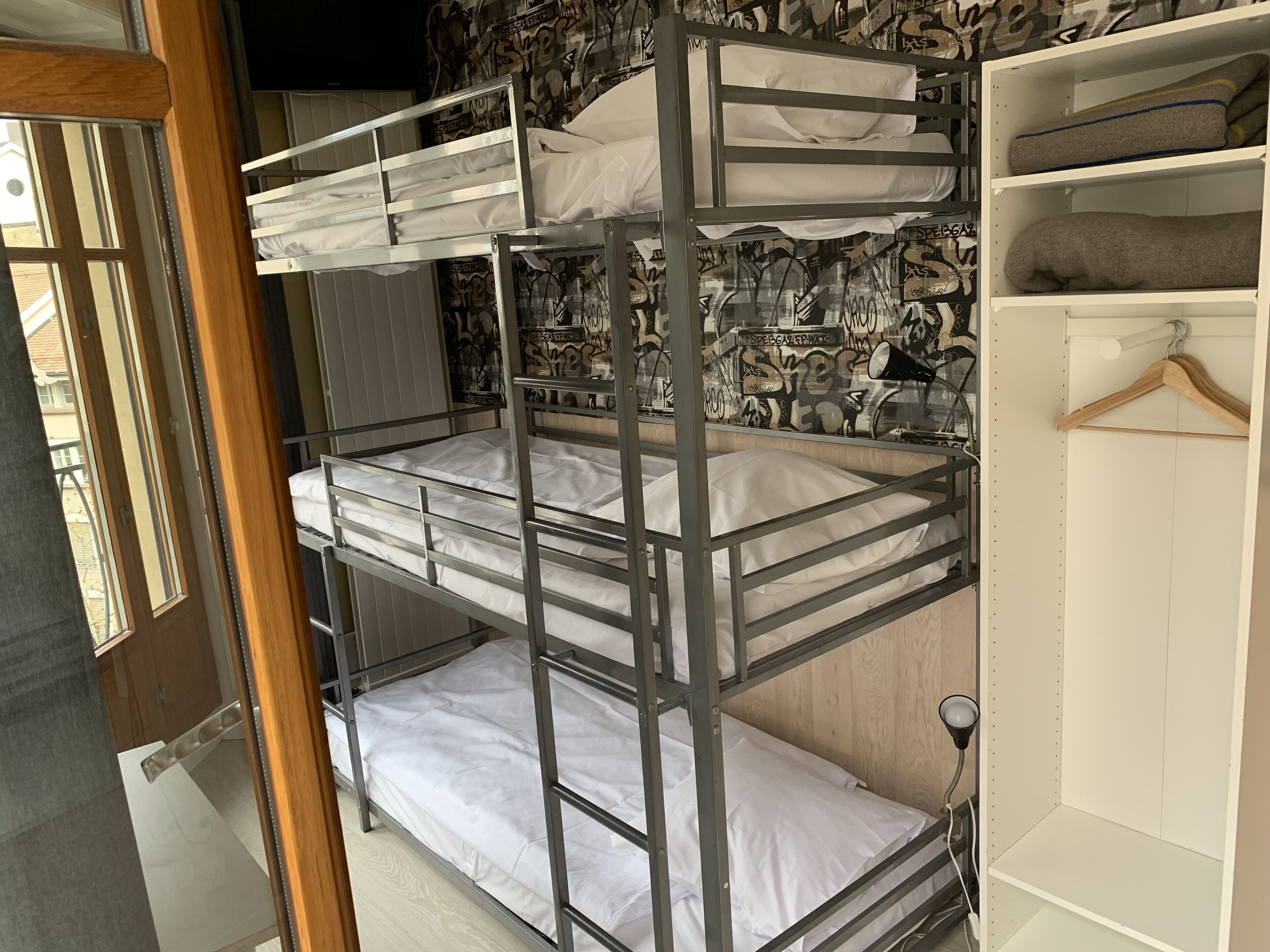 Een slaapkamer met een stapelbed, een muur met graffiti, een houten deur en een witte garderobe.