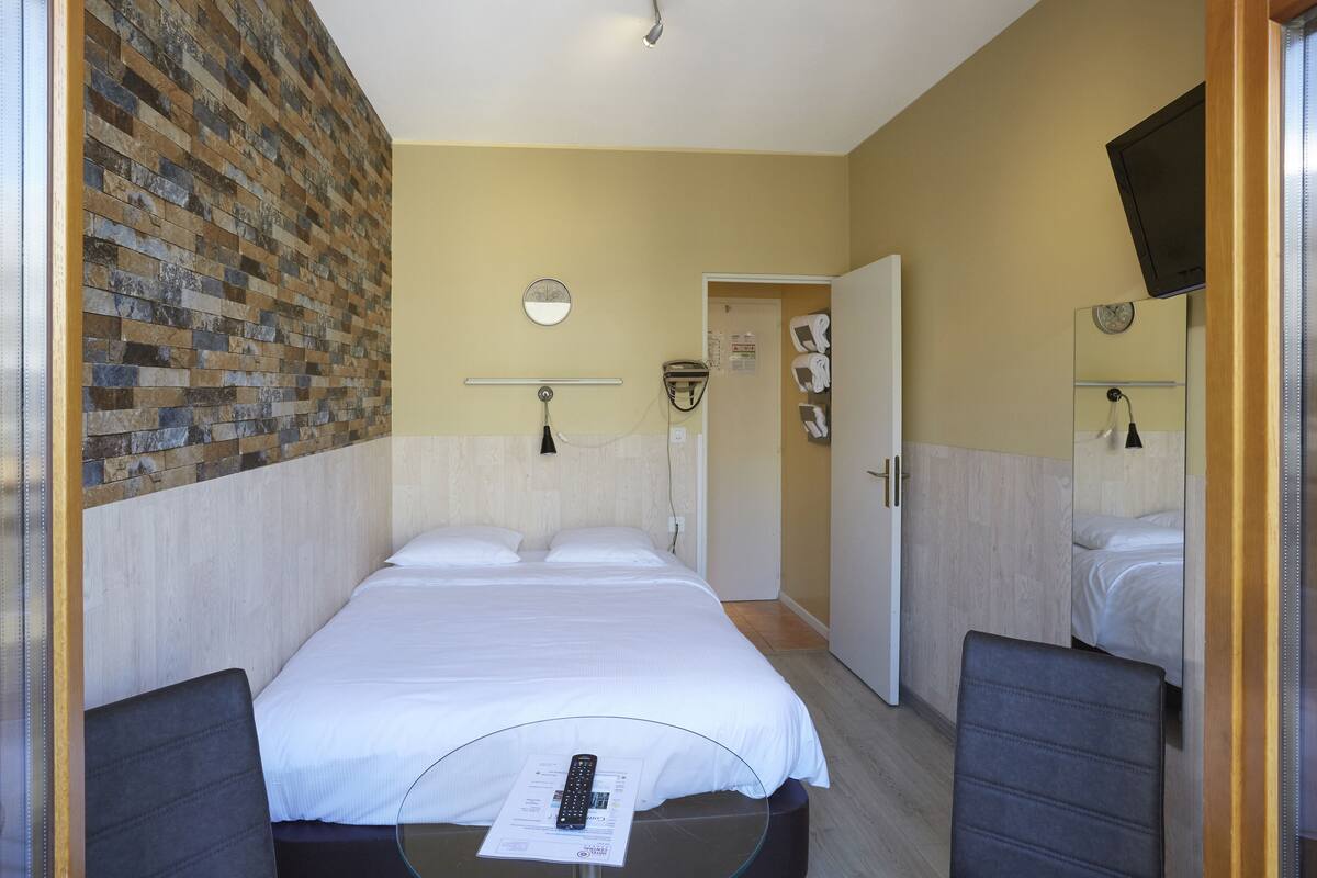 Ett hotellrum med en stor säng, två sängbord, en spegel och en tv som är monterad på väggen.