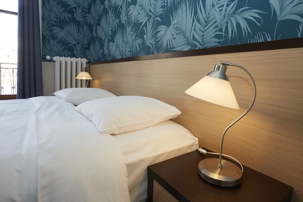 Una cama bien hecha con sábanas blancas, un cabecero de madera y una mesita de noche con una lámpara.