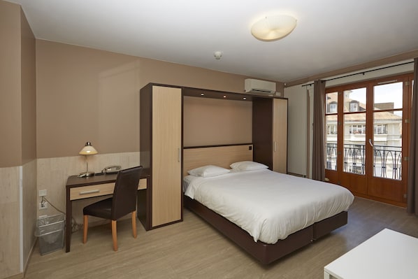 A bedroom with a bed, desk, chair, and a view of the outside. - Hotel Central (Geneva)