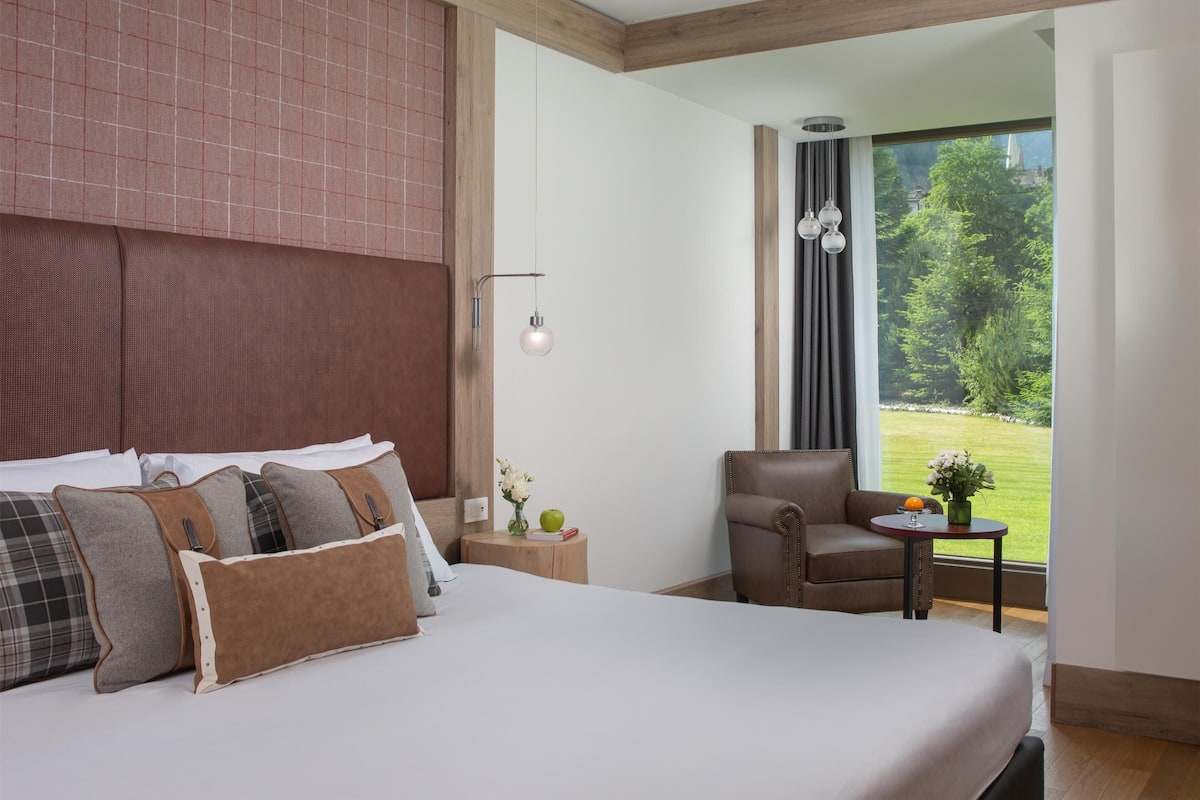 Een hotelkamer met een groot bed, een stoel, een tafeltje en uitzicht op groen.