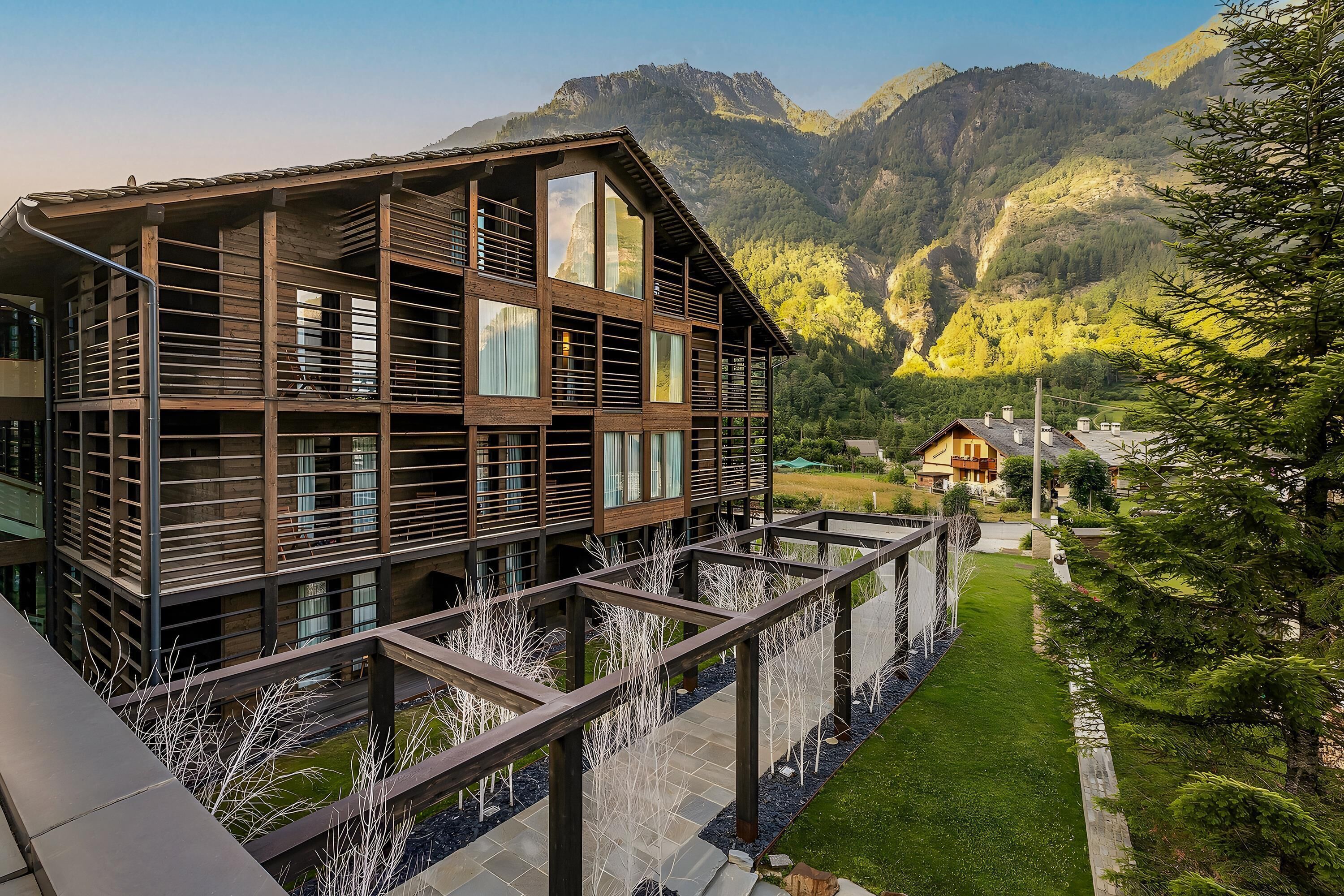 A modern multi-story building with large windows and balconies, set against a mountainous backdrop.