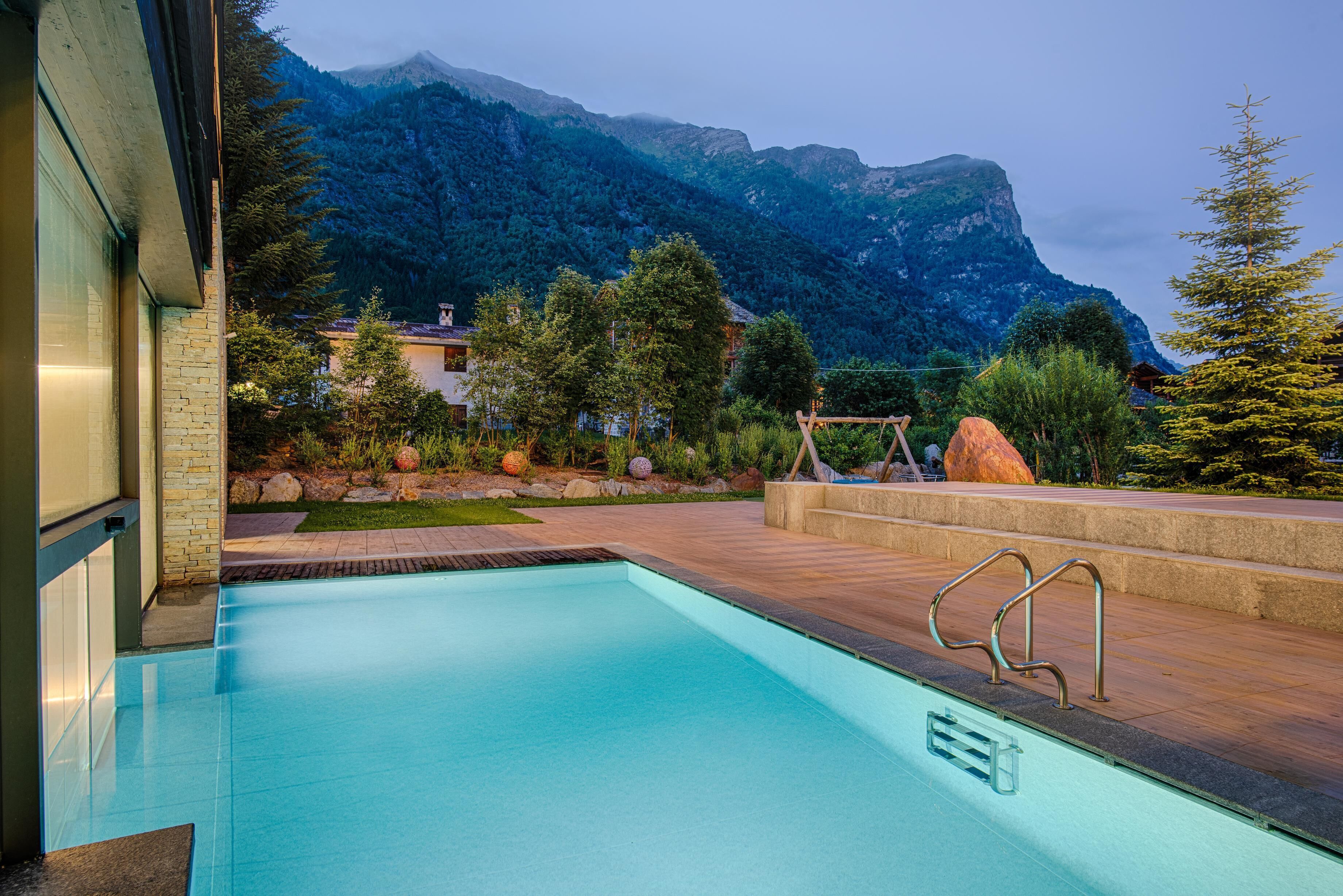 A swimming pool with a view of mountains, surrounded by a landscaped garden and a wooden deck.